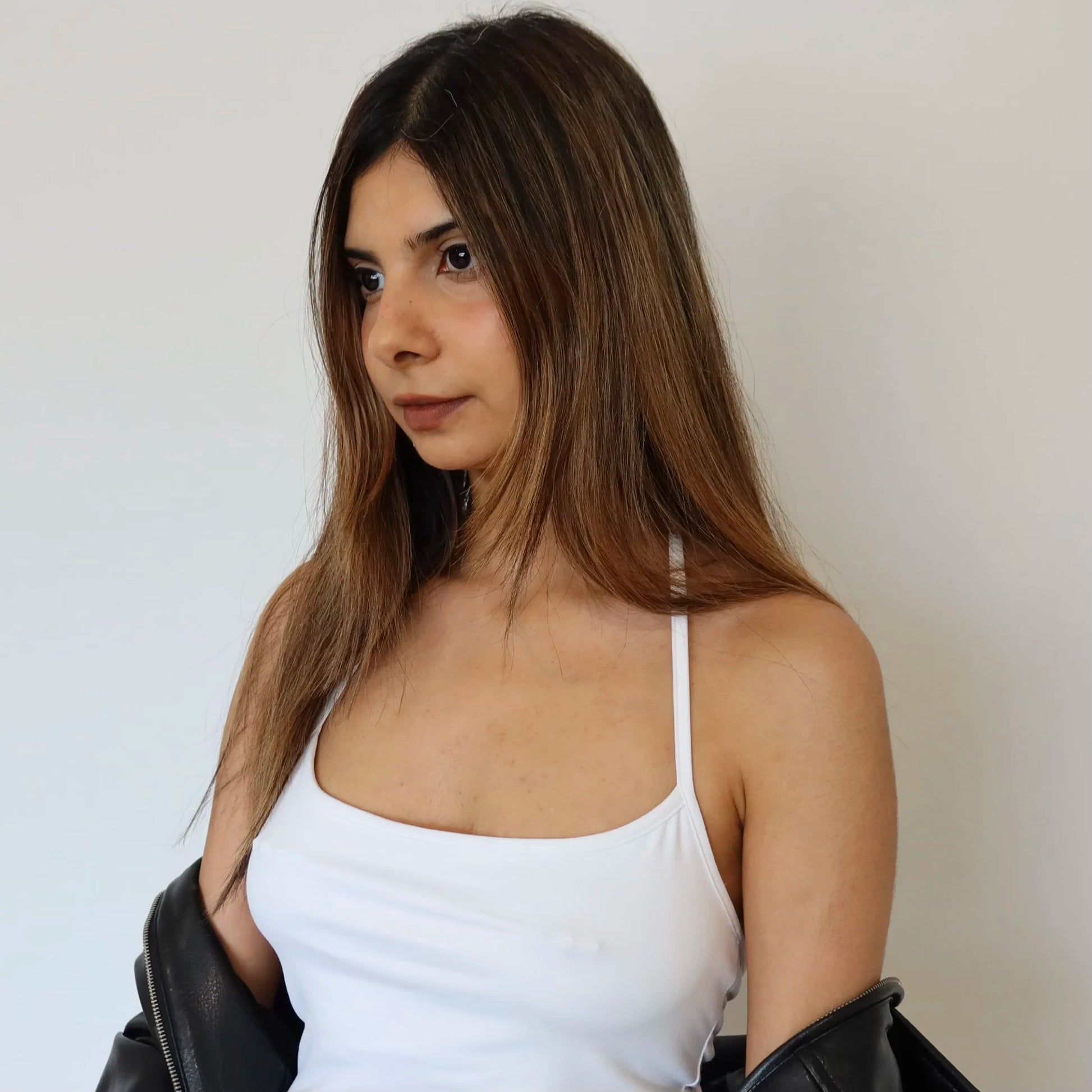 Woman wearing nip stories pierced nipple covers under a white tank top against a plain background